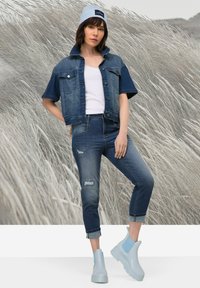 Denim-takki lyhyillä hihoilla, valkoinen toppi, kuluneet farkut ja vaaleansiniset nilkkurit. Pehmeä tuttujan tuntu, rento muotoilu, yhtenäinen sininen väriharmonia.