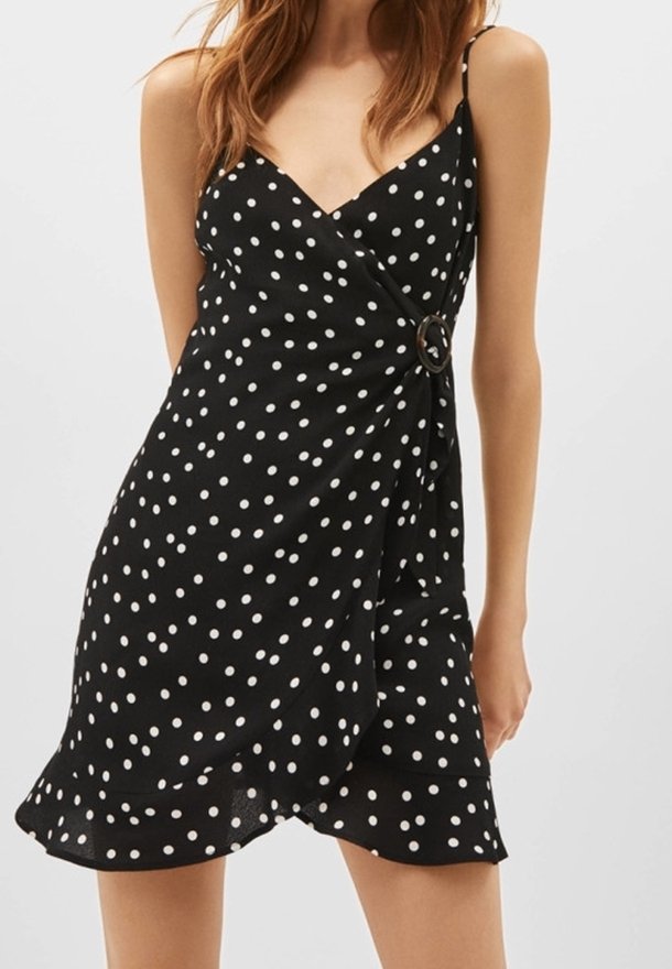 Svart klänning med prickar i polka, med omslagdesign, justerbara spaghettiband, sidoringdetalj och en volangkant. Tillverkad av lättviktig tyg.