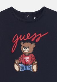 Mørkeblå T-skjorte med et bære-grafikk iført en rød genser med et hvitt trekantlogo og blå jeans; rund hals, myk stoff.