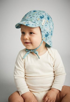 Toddler wearing a long-sleeve cream onesie and a light blue animal-patterned sun hat tied under the chin, sitting and looking to the side.