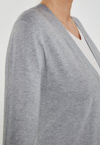 Cardigan gri, cu un tricot moale și ușor, având un decolteu în V. Țesătura are o textură netedă și un finisaj subtil.