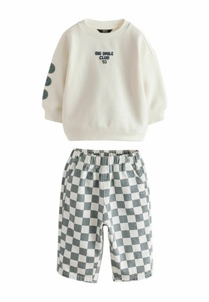 Cremefarvet sweatshirt med lange ærmer med teksten "Big Smile Club '82" og smileys på ærmet, kombineret med grå og hvide ternede shorts.