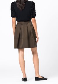 Černý top s volánovými rukávy, olivová plisovaná sukně a černé baleríny. Sukně má hladkou strukturu a sahá nad kolena.
