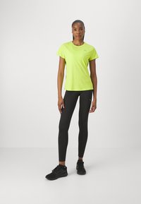 Camiseta atlética de manga corta amarilla brillante combinada con leggins ajustados negros y zapatillas negras, con un logo en la camiseta.