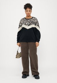 Juodas ir grietinėlės spalvos megztinis su leopardų raštu, turintis zigzago dizainą. Derinamas su rudais plačiapročiais šortais ir mažąją zebra rašto rankinę.