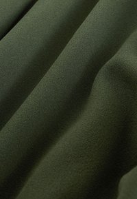 Grönt tyg med en texturerad, mjuk yta, som har subtila vågor och veck, vilket indikerar flexibilitet och fallande egenskaper.