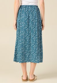 Vihreä midi-hame, joka on valmistettu keveästä kankaasta, jossa on valkoinen kukkakuosi, elastinen vyötärö ja kerroksellinen helma, yhdistettynä vaaleanbeigeihin espadrillikenkiin.