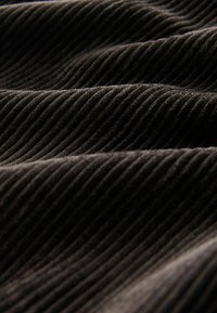 Schwarzer Cordstoff mit vertikalen Rippungen, der eine sanfte Textur mit leichtem Glanz aufweist und in sanften Wellen fällt.