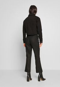 Zkrácená černá džínová bunda s límcem, dlouhými rukávy a knoflíkovými manžetami, spojená s černými kalhotami s vysokým pasem a kotníkovými botami.