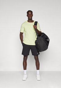 Light green short-sleeve t-shirt with "Champion" logo, black shorts, white sneakers, and a black sports bag with shoulder strap.