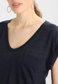 Navy blue V-neck T-shirt made of lightweight fabric, featuring rolled sleeves and a small front pocket for added detail.