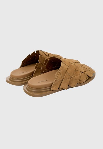 Sandalias de ante marrón tejido, tipo slip-on, con suelas planas apiladas, costuras visibles y diseño de punta cerrada, vistas desde un ángulo lateral trasero.