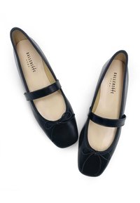 Bailarinas de cuero negro con punta redondeada, tacón plano y un lazo decorativo. Cuentan con una correa en el empeine y forro beige.