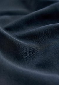 Granatowy materiał o gładkiej fakturze, z delikatnymi diagonalnymi prążkami, ułożony w łagodne fałdy, które podkreślają jego opadanie i miękkość.