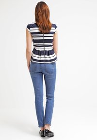 Laivastonsininen ja valkoinen raitapaita peplum-hihalla, takakäyttölukolla, yhdistettynä sinisiin farkkuihin ja mustiin kenkiin, nähtynä takaa.