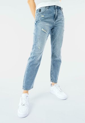 Jeans in denim chiaro, distressati, con vestibilità dritta, caratterizzati da strappi e un classico design a cinque tasche. Abbinati a sneaker bianche.