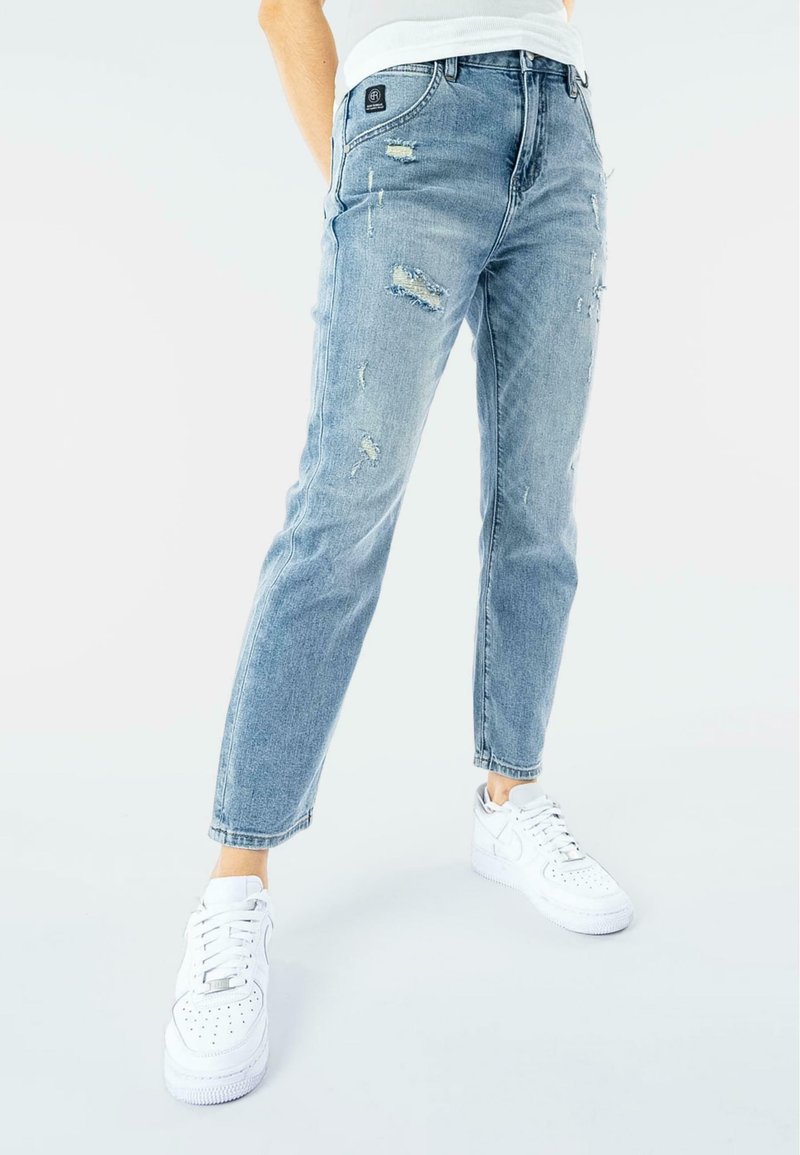 Jeans in denim chiaro, distressati, con vestibilità dritta, caratterizzati da strappi e un classico design a cinque tasche. Abbinati a sneaker bianche.