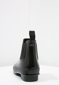 Czarny gumowy botek za kostkę z elastycznymi panelami po bokach, teksturowanymi żebrowaniami na pięcie oraz pętelką z tyłu ułatwiającą zakładanie.