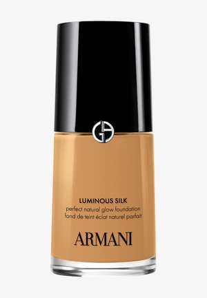 Luminous Silk Foundation in einer Glasflasche mit schwarzem Verschluss, goldener Flüssigkeit im Inneren und klarem Boden mit eingeprägtem Text und Logo.