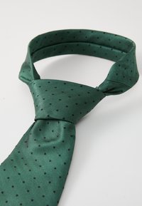 Cravate en soie verte avec un motif en chevrons et de petits points noirs, dotée d'une texture lisse et d'une forme triangulaire standard.