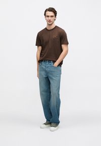 Tricou maro din bumbac cu un mic logo imprimat pe piept, asortat cu blugi drepti, de culoare bleu deschis, și adidași verzi.