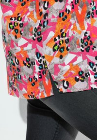 Top colorato con un motivo astratto di forme rosa, arancione e grigie, impreziosito da macchie leopardate nere e turchesi. Fessure laterali visibili.