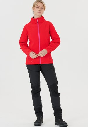 Rode softshell jack met een hoge kraag en een roze rits, gecombineerd met zwarte broek met meerdere ritszakken en gestructureerde accenten.