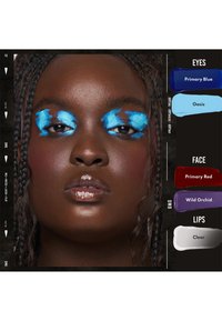 Persona di carnagione scura con capelli intrecciati, che indossa un audace ombretto blu astratto, blush rosso e labbra lucide con lucido trasparente, accanto a campioni di colore per il trucco.
