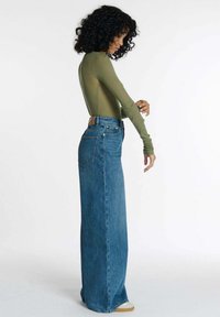 Groene langekuipe bodysuit in combinatie met high-waisted, wijde spijkerbroeken in blauw denim. De spijkerbroeken hebben een achterzak en zijn vloerlengte.