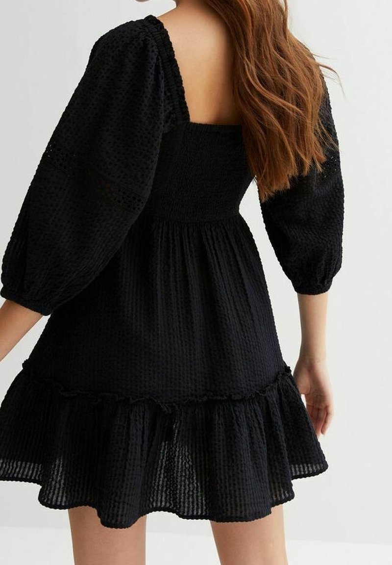 Svart kort klänning med puffärmar, strukturerad tyg och utställd nederkant. Har fyrkantig halsringning och rynkad midjedesign.