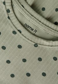 Πράσινο ριμπ ύφασμα μπλουζάκι με σκουροπράσινες πουά, με στρογγυλή λαιμόκοψη και την ετικέτα της μάρκας "name it" μέσα στο γιακά.
