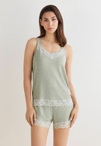 Lichtgroene loungewear set met een mouwloze top en shorts, beide voorzien van delicate witte kanten randen langs de randen en de halslijn. Soepele stof.