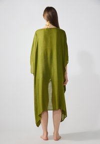 Cubierta estilo kimono de color verde oliva, hecha de un tejido ligero y transparente, con un corte suelto y un diseño de dobladillo asimétrico, adornada con un lazo en el cuello.