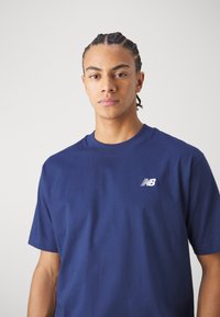 T-shirt en coton bleu marine avec un col rond et des manches courtes, arborant un petit logo "NB" blanc sur la zone gauche de la poitrine.