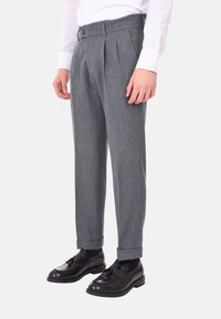 Pantaloni di lana grigi con pince, caratterizzati da una texture liscia e un design aderente, abbinati a scarpe eleganti nere.