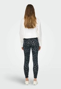 Svarta leggings med ett lejonsmönster, tillverkade av stretchigt tyg, tillsammans med en vit löst sittande skjorta och ljusa skor.