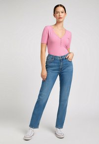 Body rosa de canalé con escote en V y detalles de botones combinado con jeans de mezclilla azul de tiro alto y zapatillas blancas.