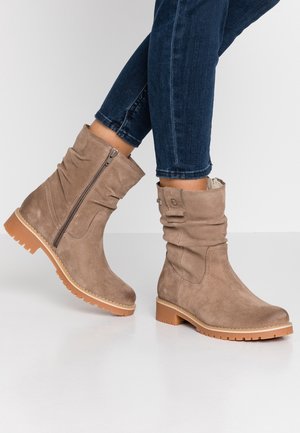 Taupe suede mid-calf boots with side zipper and rubber lug sole worn with rolled-up dark blue jeans on a white background.