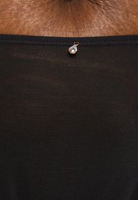 Tela negra con textura de malla, con un escote suave y un acento decorativo en forma de gota cerca de la costura.