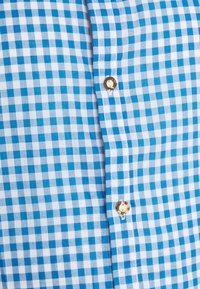 Tissu à carreaux bleus et blancs avec deux boutons visibles le long de la couture, montrant les détails en gros plan du devant d'une chemise.