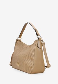 Bolso de mano marrón con textura trenzada, detalles en cuero suave y una etiqueta de hardware dorado. Cuenta con una sola correa para el hombro y una correa cruzada ajustable.