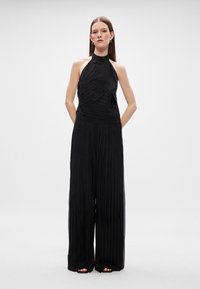 Μαύρο πλεγμένο  jumpsuit με αμάνικο σχεδιασμό, διαθέτοντας υφασμάτινη υφή και φαρδιές παντελόνες. Ο λείο κορσές μεταβαίνει σε ρυακωτά παντελόνια.