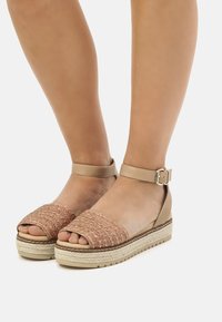 Sandali espadrilles beige con tomaia in pesca tessuta e texture, punta aperta, cinturino alla caviglia e suola impilata con texture.