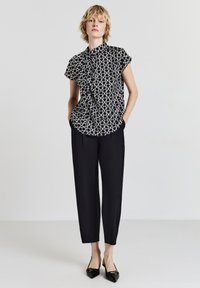 Blusa a righe bianco e nero con colletto alto, abbinata a pantaloni neri e ballerine appuntite, che mostrano una vestibilità rilassata e una texture liscia.