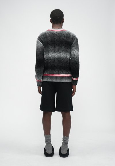 Hallhalli soe kudum sweater hallide ja valgete detailidega, kombineeritud mustade lühikestega. Mudel kannab halli sokke ja musti kingi.