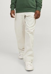 Pantaloni ampi color beige chiaro realizzati in tessuto liscio, con tasche laterali e abbinati a sneakers bianche.