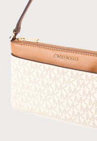 Michael Kors lynlomme i creme med monogrammønster og brune læderkanter. Har et slankt design og en lynlås i guldfarve.