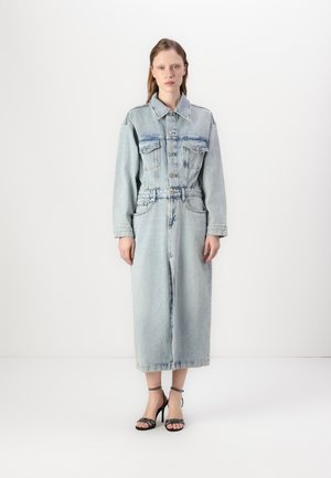 Lys blå denimjakke-kjole med lange ermer, to brystlommer, knappestenging og cinch liv, sammen med svarte høyhælte sandaler.