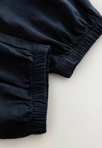 Mörk marinblå tyg med elastiska muddar, visar närbild av textur och samlade sömmar på lättviktigt material.