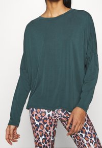 Mörk teal långärmad topp i mjukt tyg med avslappnad passform. Matchad med leggings i rosa leopardmönster med en glänsande yta.